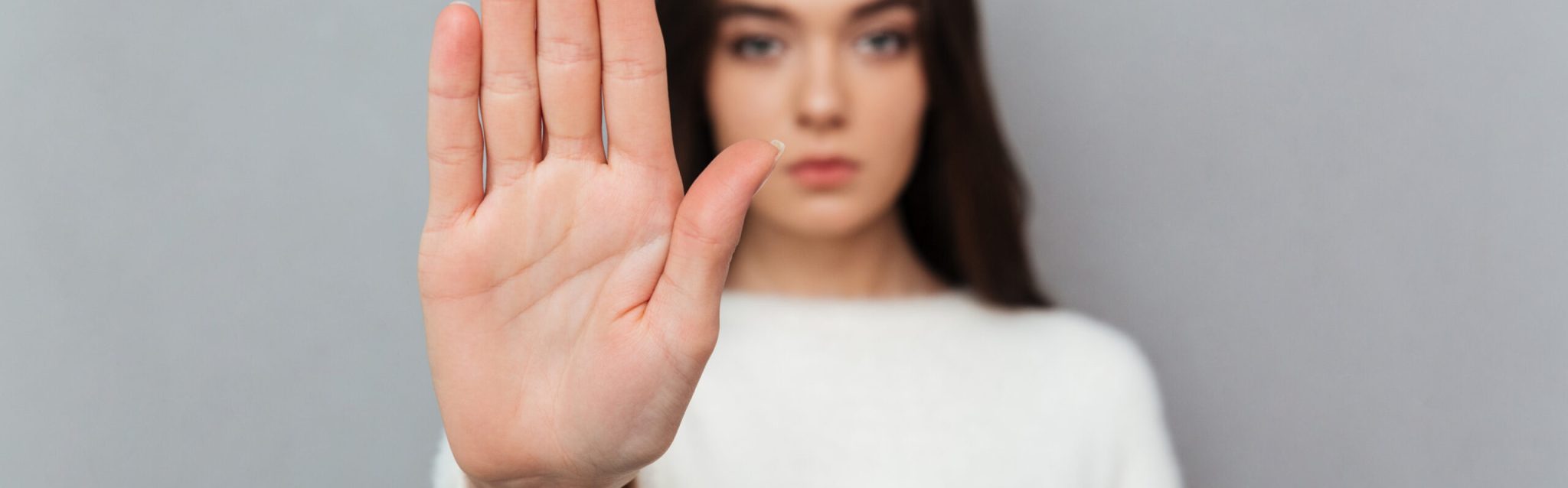 Close up portrait of a woman showing stop gesture with her palm isolated over gray background