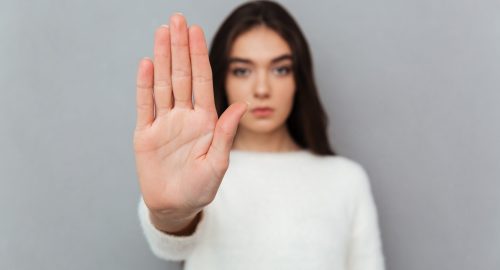 Close up portrait of a woman showing stop gesture with her palm isolated over gray background