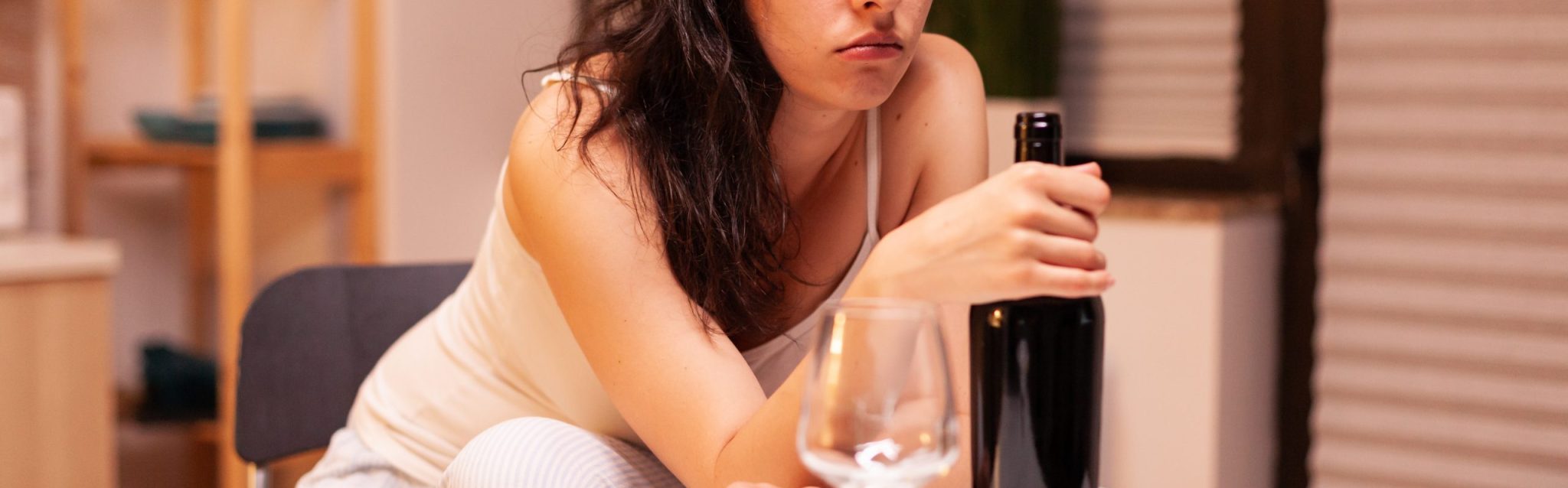 Lonely woman holding a bottle of red wine. Unhappy person suffering of migraine, depression, disease and anxiety feeling exhausted with dizziness symptoms having alcoholism problems.